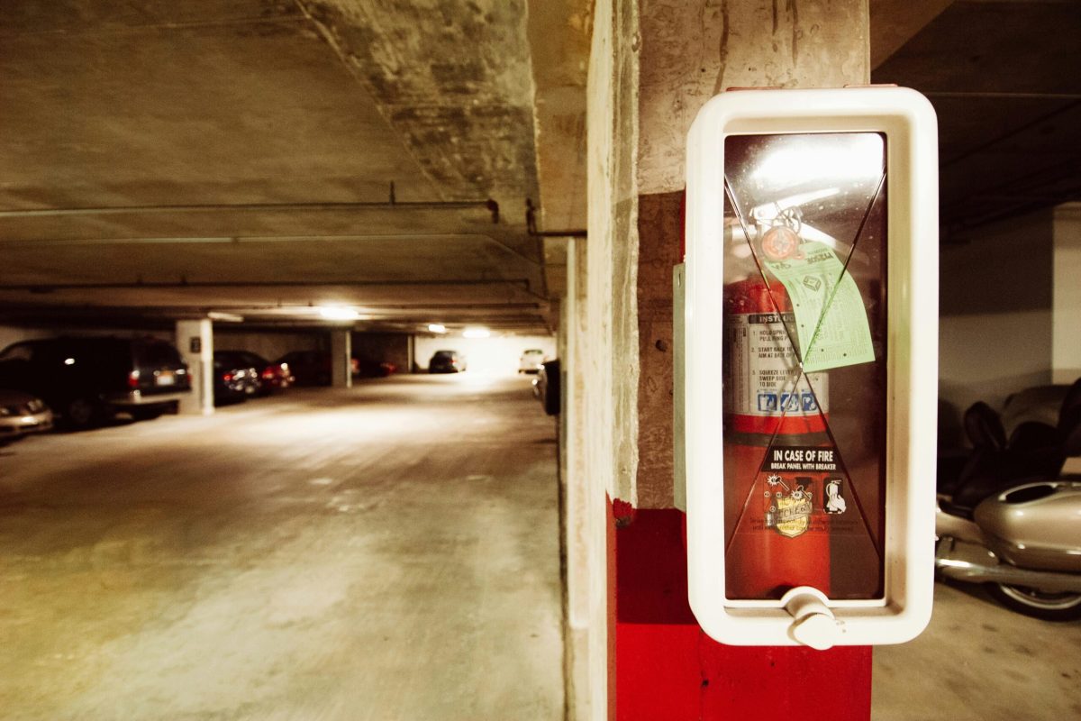 Fire extinguisher in an underground parking garage with parked cars.